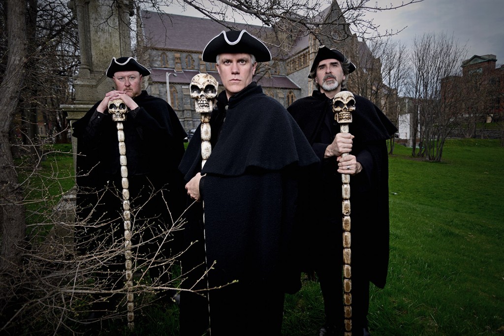 A group of spooky-looking men stand in front of an old stone cathedral